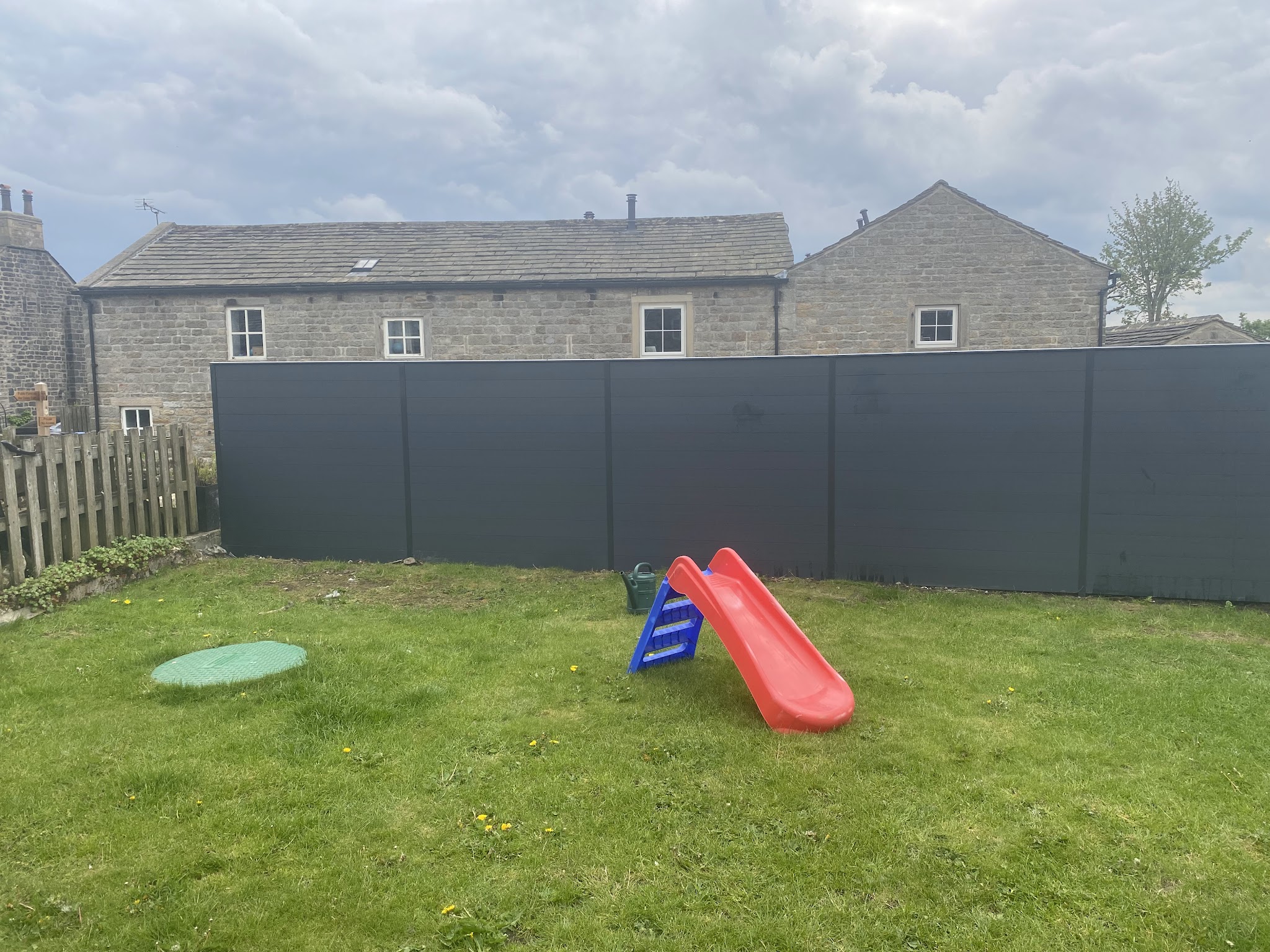 Grey fencing around a family garden with lawn and children's slide
